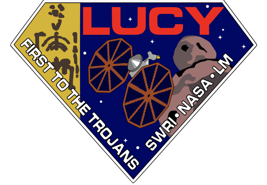 The Lucy logo. A diamond-shaped crest with LUCY written in red letters at the top. In white letters, "First to the Trojans" and "SWRI•NASA•LM" written on the left and right sides. The probe and an asteroid are featured against a backdrop of the cosmos.
