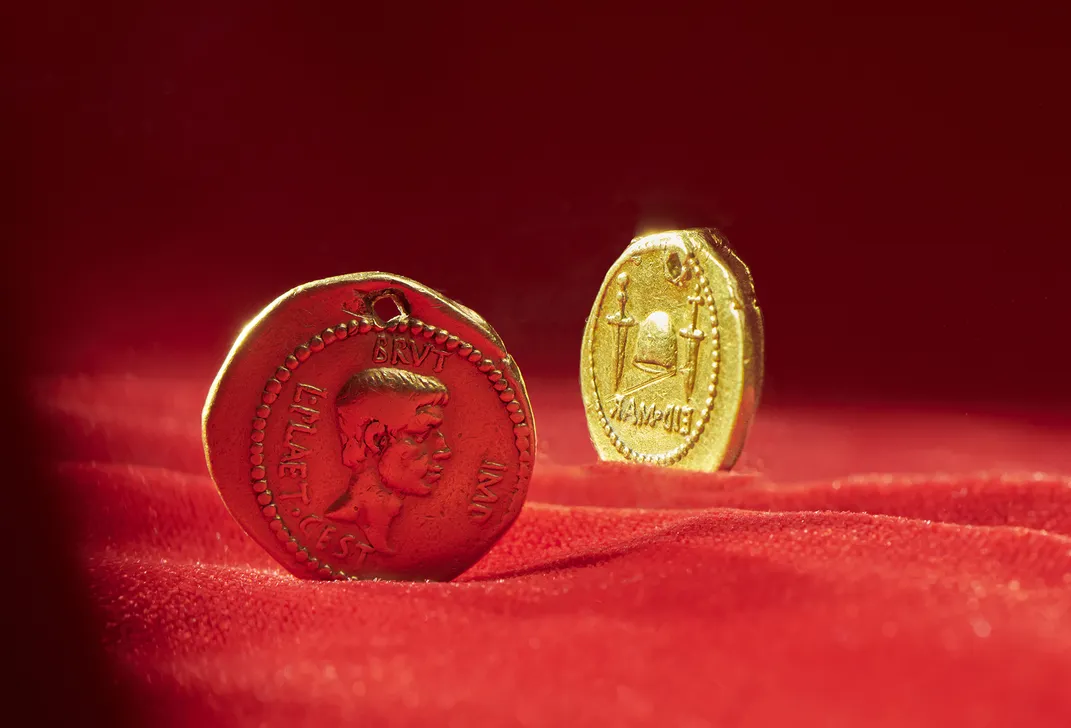 A dramatic view of the coin and its reverse, depicted as standing upright on a red cloth and framed by bright light and dark shadows
