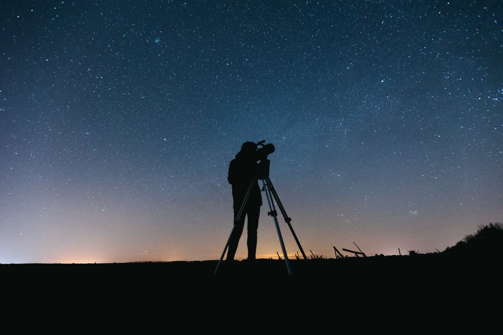 a person with a telescope in front of a starry sky