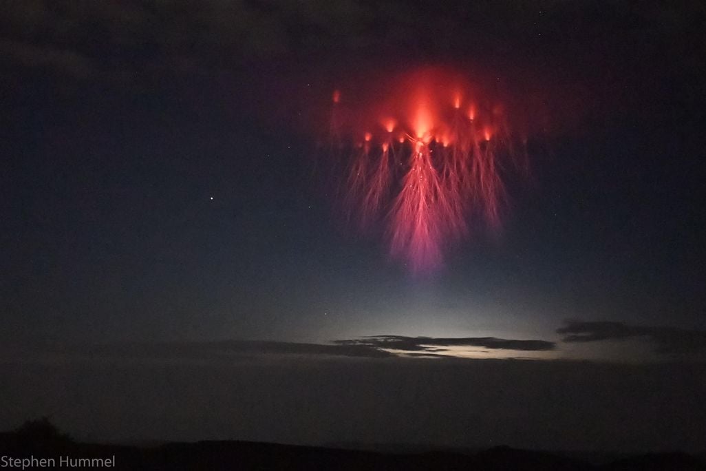 A red cloud of light hangs in the clouds with tentacles of red lightning dangling below.