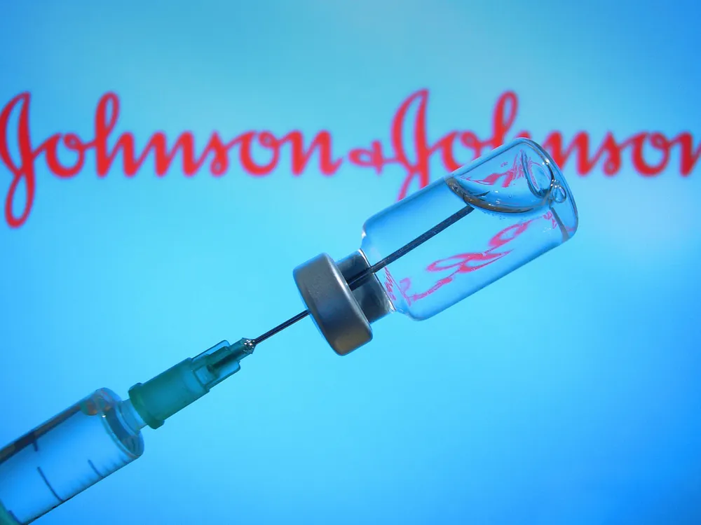 A vaccine is held up in front of a screen with the Johnson & Johnson logo