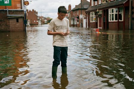 A teenage boy sends a text message on his mobile phone as stands in the floodwater on the main street of Bentley in Doncaster.