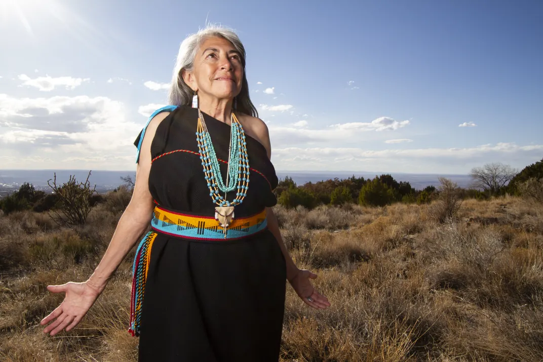 Woman with grey hair stands with arms outstretched by her sides. 