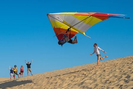 The call of the sky is strong in Kitty Hawk. Not far from where the Wright brothers first flew, student Hannah Zobel glides over sand dunes after a lesson with Luke Robinson (running) of Kitty Hawk Kites hang gliding school.