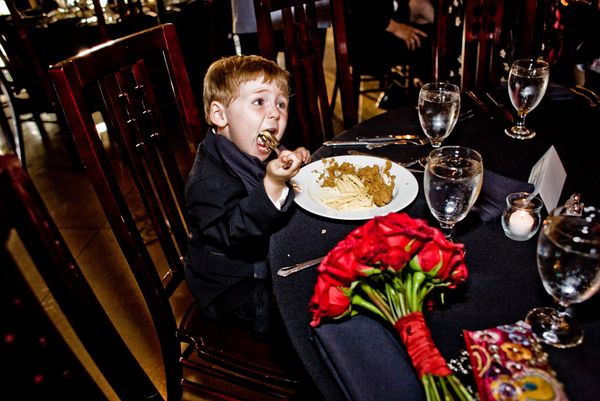 A kid takes a big bite of chicken fingers and fries at a wedding reception. thumbnail