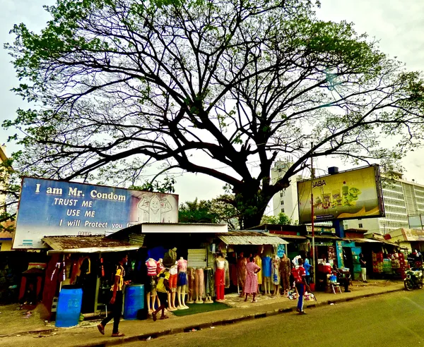 An Outdoor Street Clothing Market Framed by Charming Novel Billboards and a Tree thumbnail
