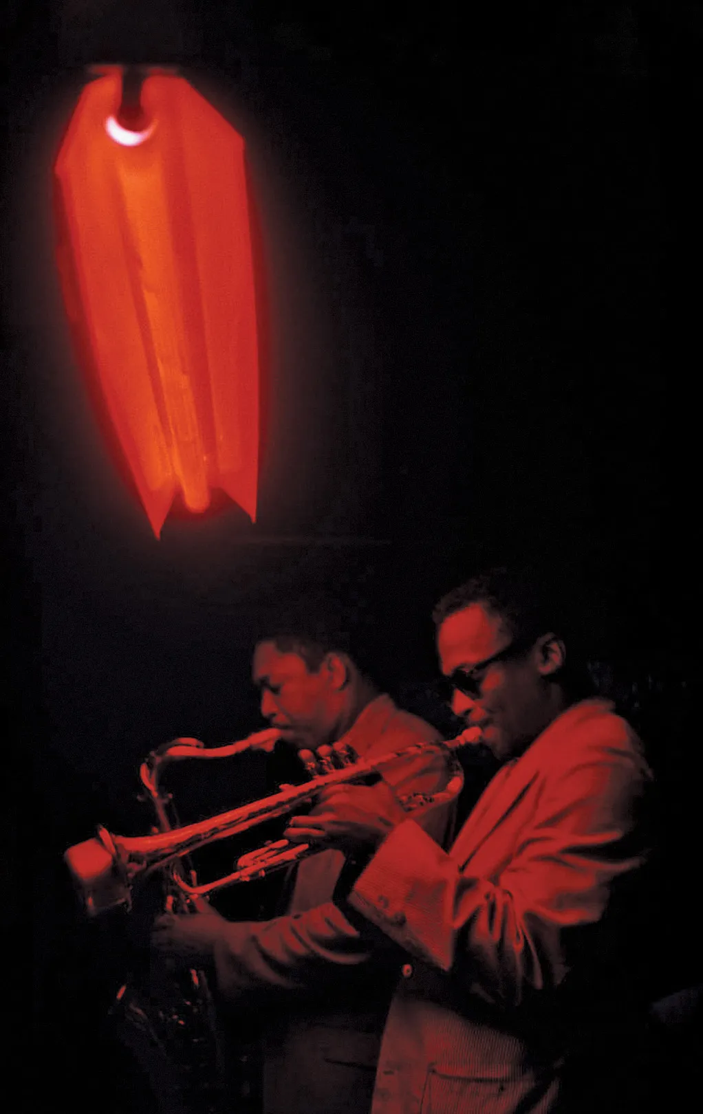 a red toned image of two musicians playing the clarinet and trumpet
