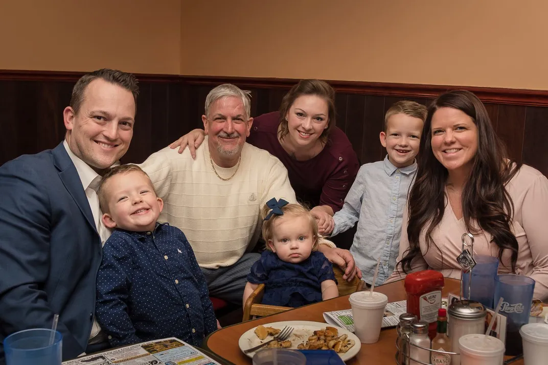 A family young children gather around a dinner table smiling