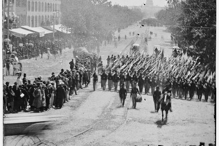 An infantry unit with bayonets marched down Pennsylvania Avenue in May 1865. They are followed by three ambulances.