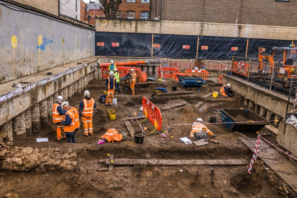 men and women in safety gear at construction site uncovering underground remnants of building