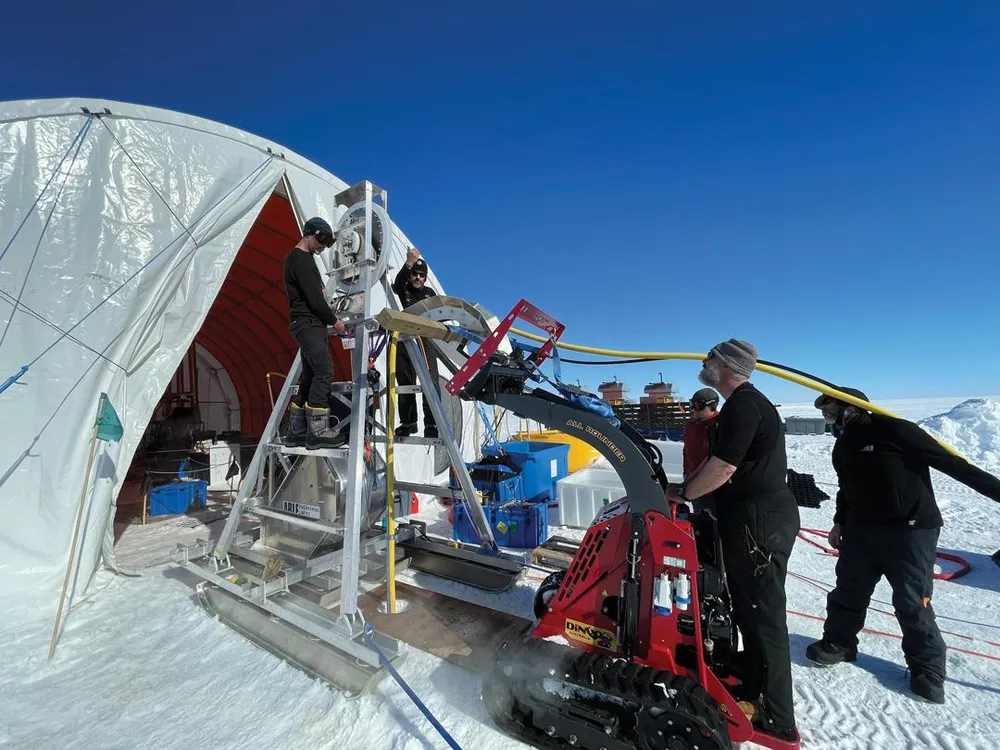 An image of reseachers gathered outside a tent using equiptment to drill a hole in ice