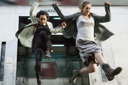 The protagonist, Tris (Shailene Woodley), and her friend Christina (Zoë Kravitz) jump from a train running through post-apocalyptic Chicago in a scene from the film Divergent. 