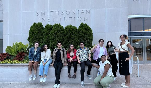 A group of student interns gather in front of a grey building