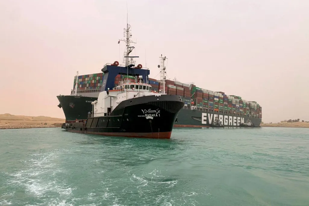 Pictures, is the shipping vessel, the Ever Given stuck on the Suez Canal. There is a tugboat pictured in front trying to pull it free