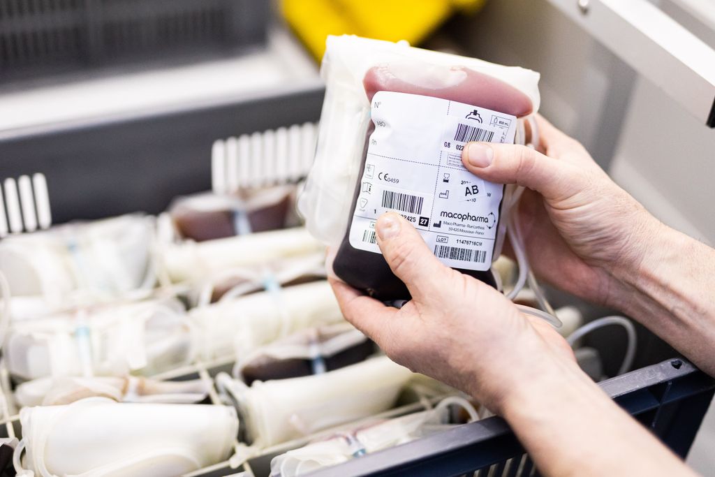 A person holds a bag of donated blood in front of a box with more donated blood