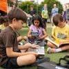A group of children sit on the grass to read silently to themselves