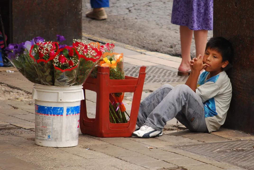 A young Hispanic boy sits on the street with flowers