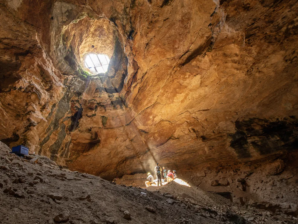 OPENER - A shaft of golden light from the cave’s mouth provides warmth as the expedition’s scientists enjoy lunch 80 feet below the opening of Natural Trap Cave.