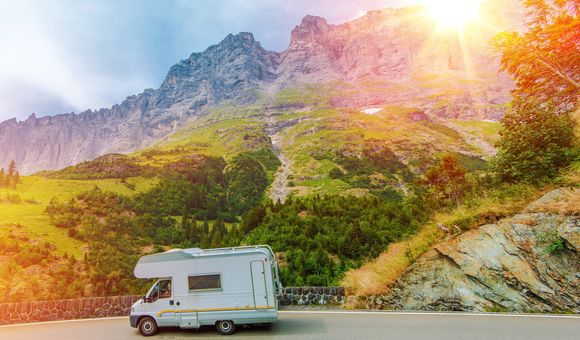 Sun shines brightly on a mountain landscape scene depicting a road with an RV