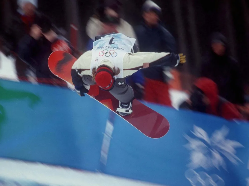snowboarder performs trick at 1998 olympics, reaching down to touch the board