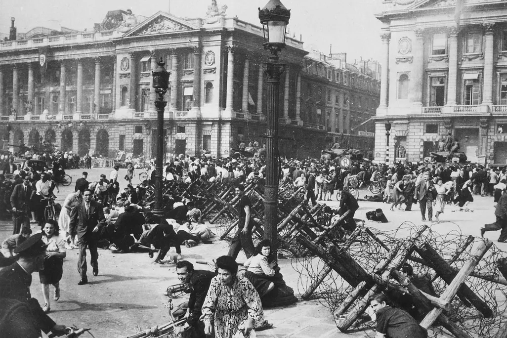 Crowds of Parisians celebrating the entry of Allied troops into Paris scatter for cover as a sniper fires from a building on the Place de la Concorde.
