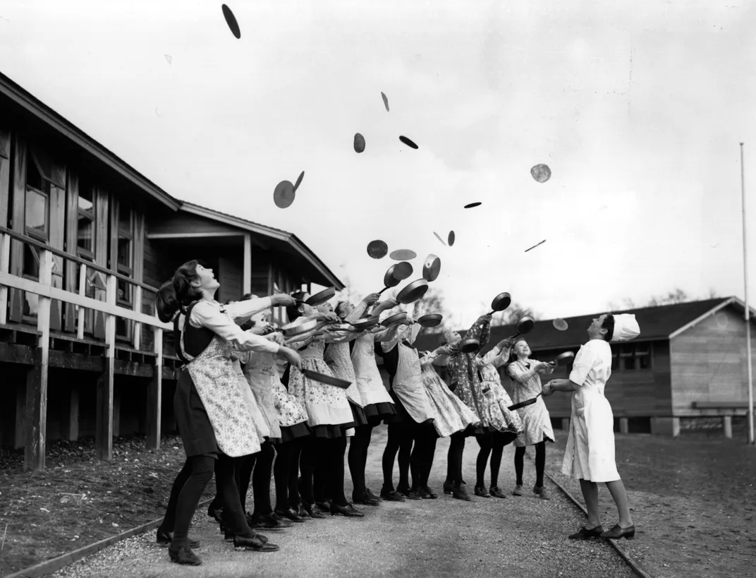 In February 1941, wartime evacuees celebrate Shrove Tuesday with a traditional pancake toss.
