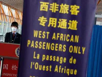 A quarantine official at Beijing's international airport stands behind a banner notifying incoming passengers from West Africa'  to use a specific lane  