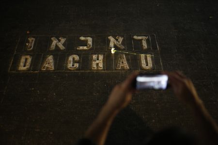 A man uses a mobile phone to photograph flowers placed on the names of concentration camps during the annual ceremony on Holocaust Remembrance Day at the Yad Vashem Holocaust Memorial in Jerusalem, Thursday, April 12, 2018.
