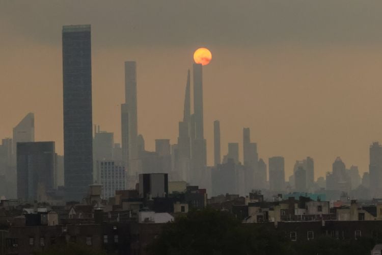 A photograph of the New York City skyline showing hazy air and the sun in the background