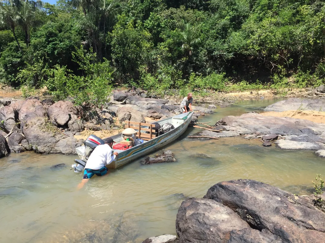 Two people pushing a small boat in a river.