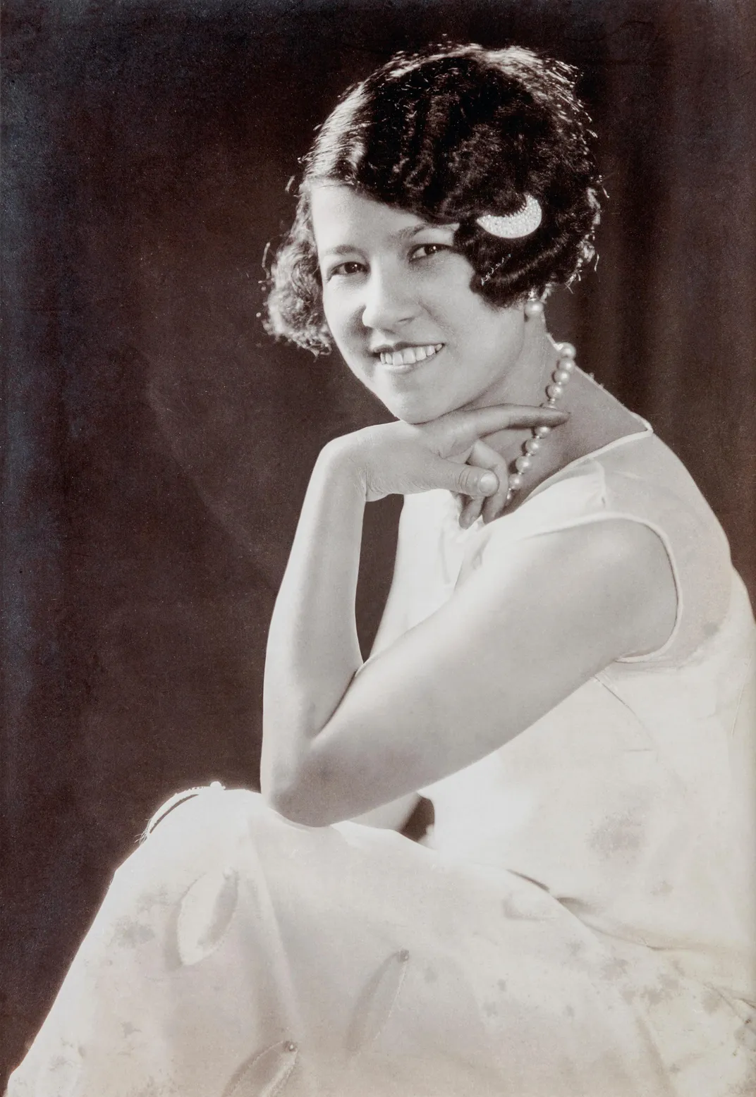A posed studio portrait of Collins, a Black woman with short cropped hair in pearls and an elegant white dress