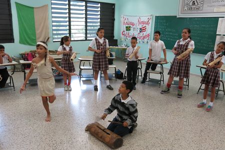 In this April 10, 2015 photo, Brayan Lopez, 9, plays a Taino wood drum while students perform a ceremonial dance in San Lorenzo, Puerto Rico. 