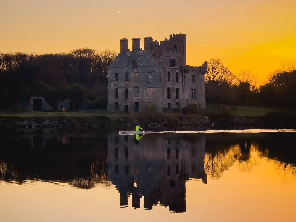 The photo was taken during golden hour at River Corrib, where a single kayaker passed by Menlo Castle.
