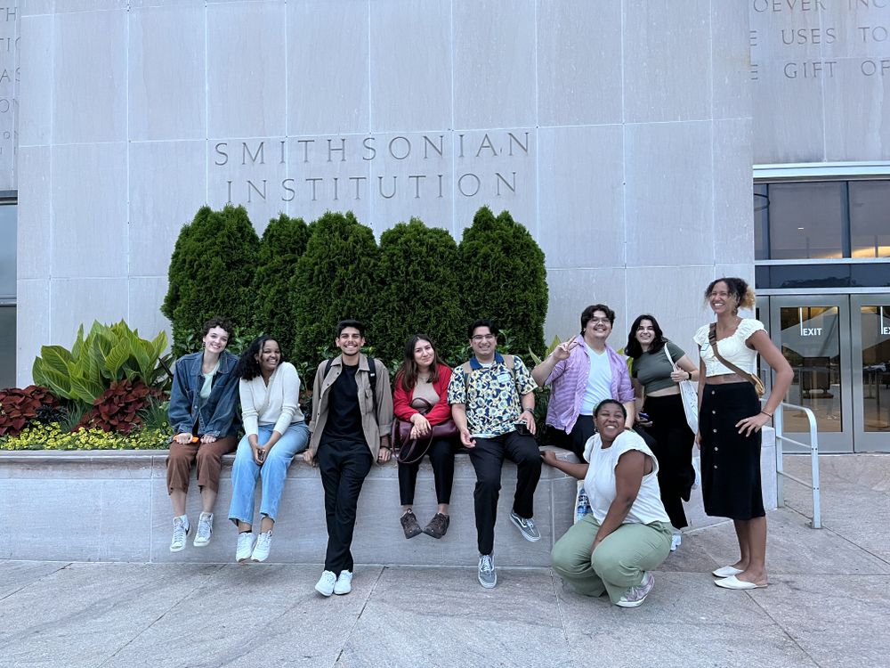 A group of student interns gather in front of a grey building