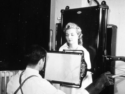 A technician takes an X-ray fluoroscope of a female patient. Fluoroscope exams delivered much more radiation exposures than modern X-rays.