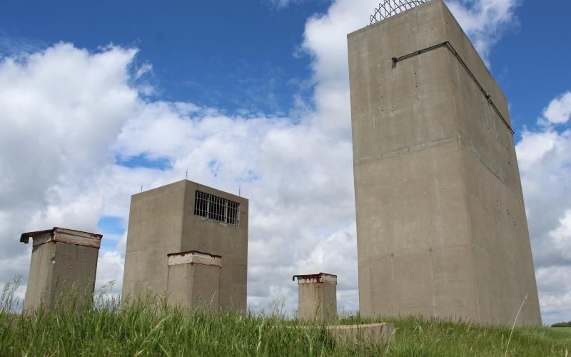 A view of four large rectangular buildings made of smooth concrete, framed against a blue sky with white, fluffy clouds