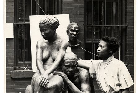 A black and white photograph of artist Augusta Savage standing next to her sculpture