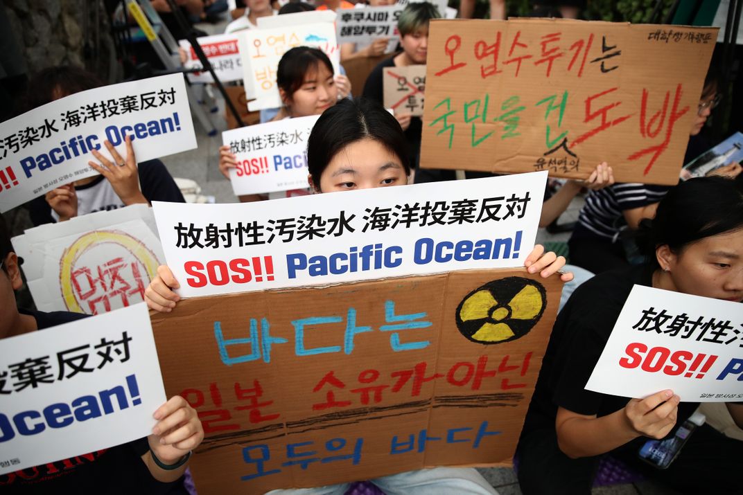 people holding signs in a protest with words in Korean; English words read "SOS!! Pacific Ocean!"