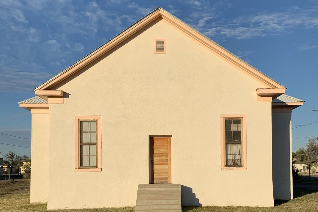 A front-on view of a simple white building with two windows on either side of a small door
