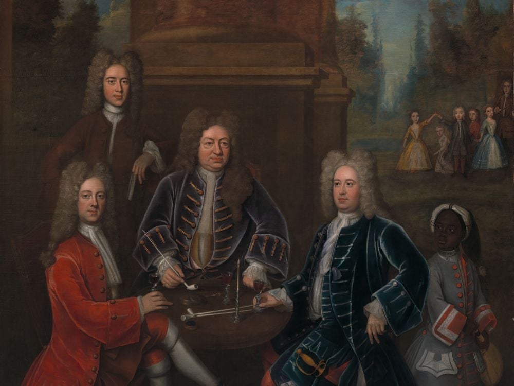 A group portrait of four white men sitting and standing around a table, smoking and drinking wine, while a small group of white children play in the distance and a Black child wearing a padlocked collar serves them wine