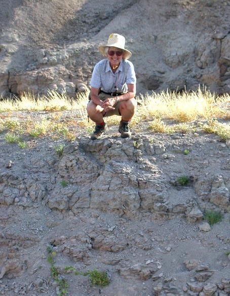 A person squatting on a rocky hill.