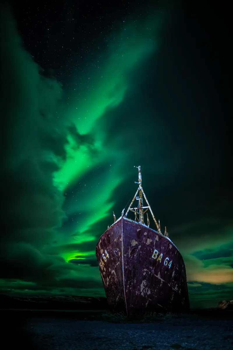 Una imagen de un barco con aurora boreal en el cielo