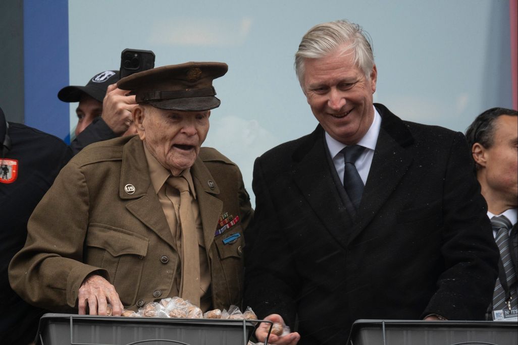 Elderly man wearing military uniform standing next to other man wearing a suit