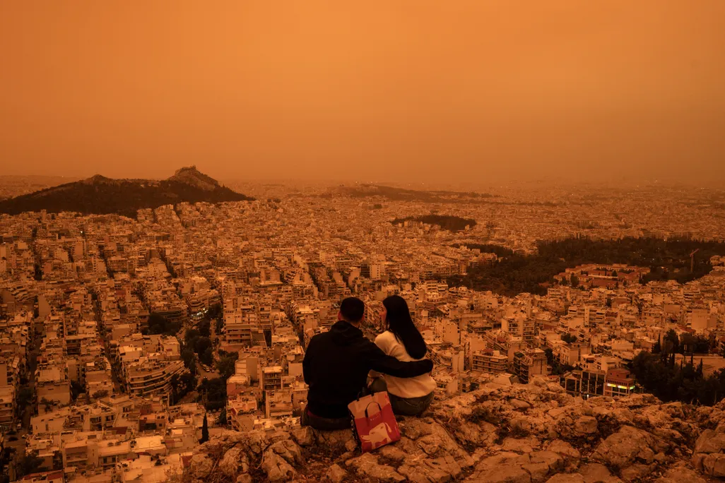 A couple sits atop Tourkovounia hill in Athens, as clouds of Saharan dust cover the capital.