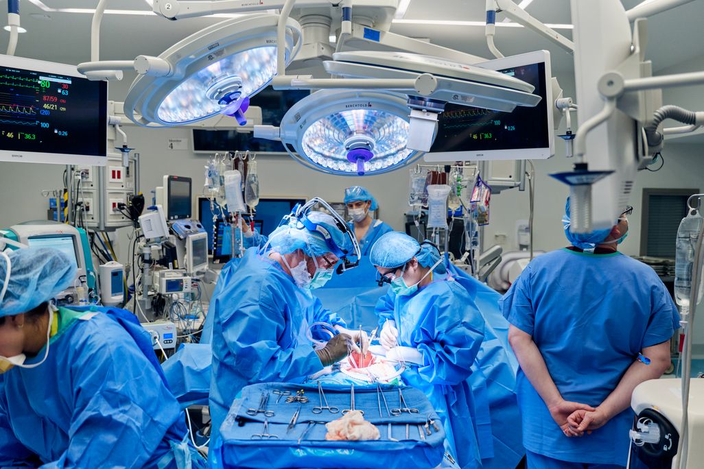 Surgeons in blue scrubs gathered around a patient on an operating table