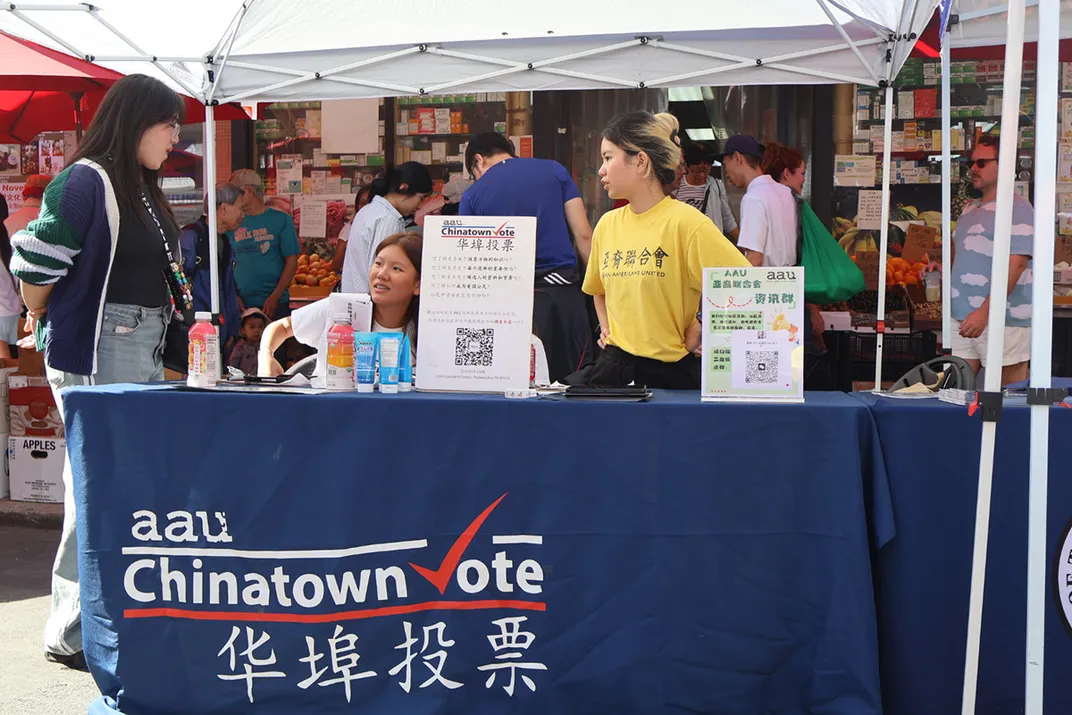 Three people chat behind an information table with banner text: AAU Chinatown Vote, plus Chinese characters.
