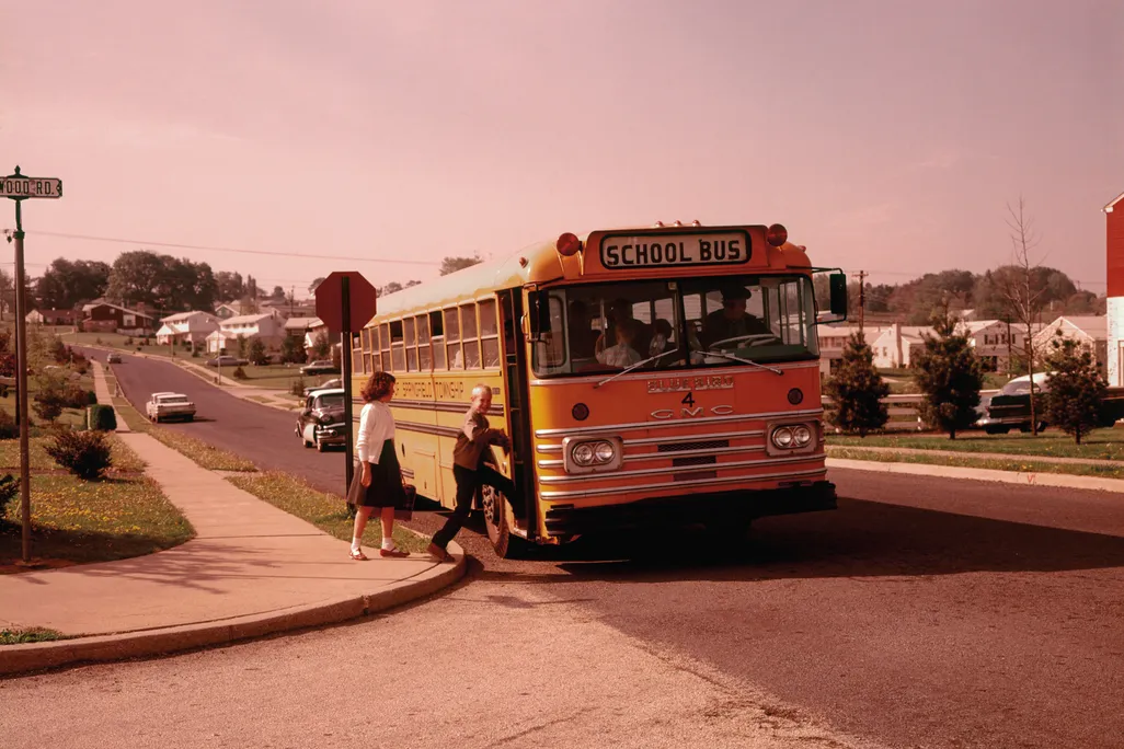 kids getting on a school bus in a suburban neighborhood in the 1960s