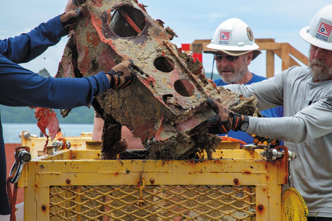 The crew unloads a component of the airplane’s internal structure from a basket recently brought up from the ocean floor.