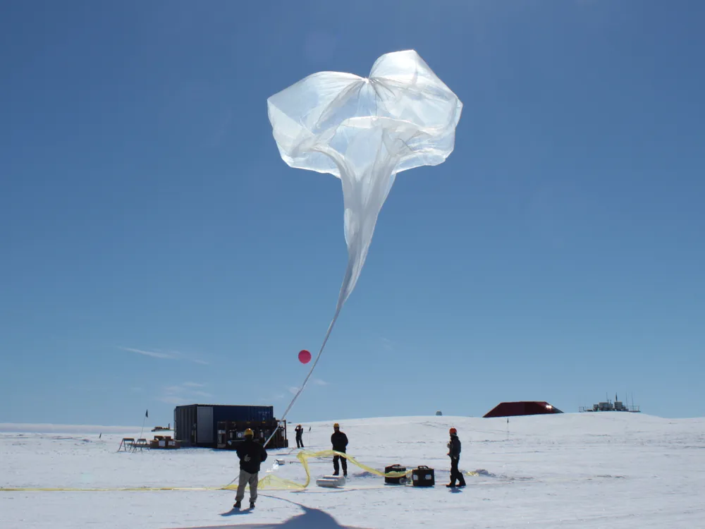 scientists inflate a large white balloon on an icy landscape