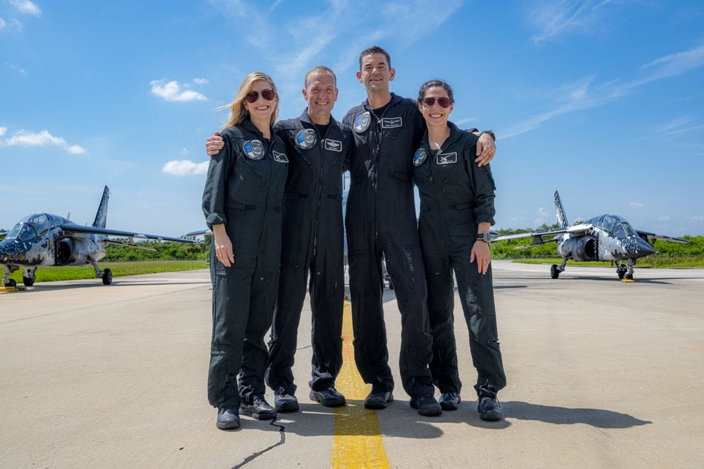 Four people in blue suits stand on a runway
